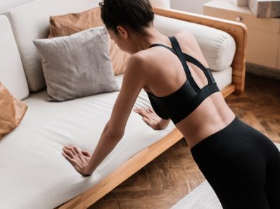 An active adult woman performs push-ups indoors using a sofa for support, emphasizing a healthy lifestyle.